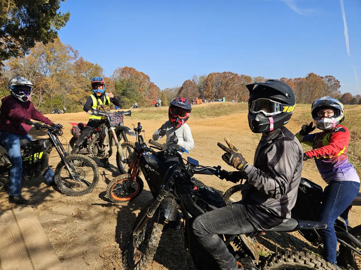 A family group on electric motos and a dirt bike giving thumbs up by the track