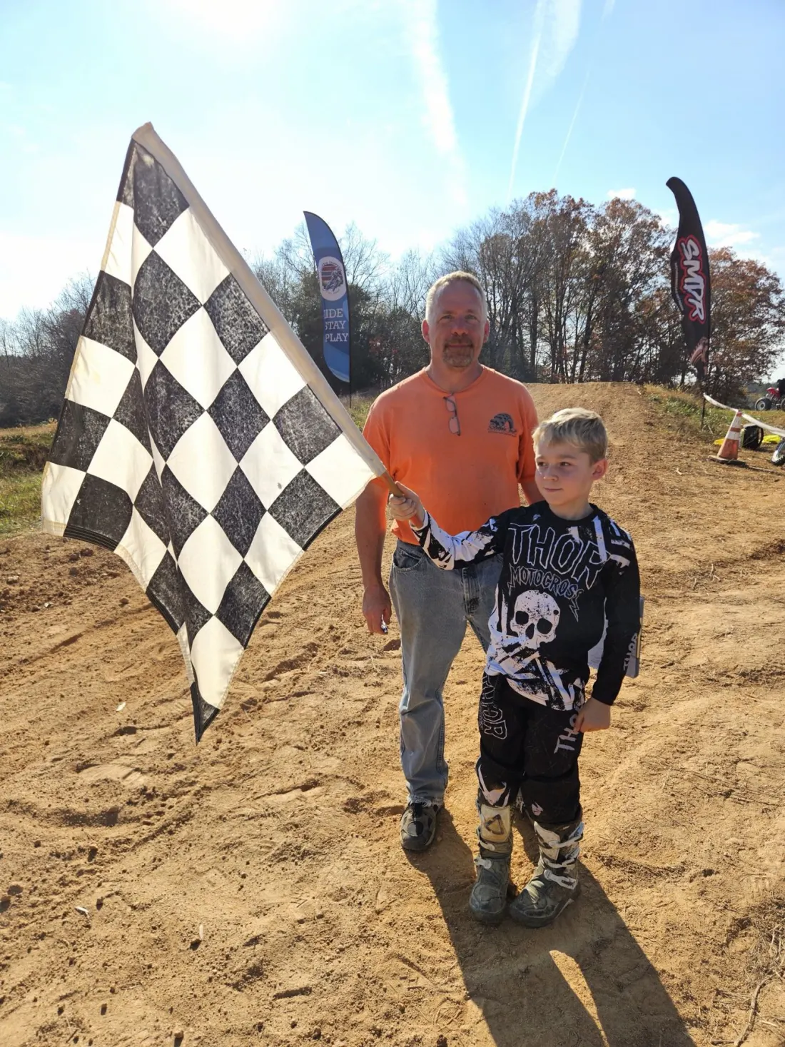 A young rider in motocross gear holds a checkered flag on the track
